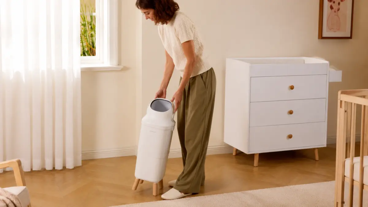 Mulher desloca um cesto branco para fraldas no quarto infantil.