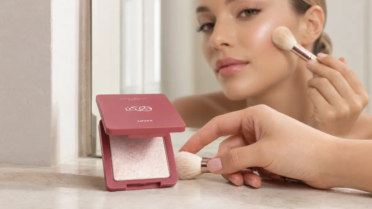 Mulher aplica LOVRO Highlighter Paste com um pincel na ma&ccedil;&atilde; do rosto