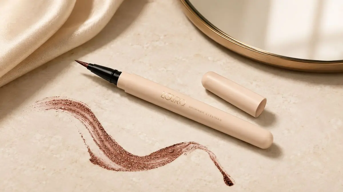 Lovro Shimmer Eyeliner 01 Chocolate com um pincel fino sobre fundo rosa-claro