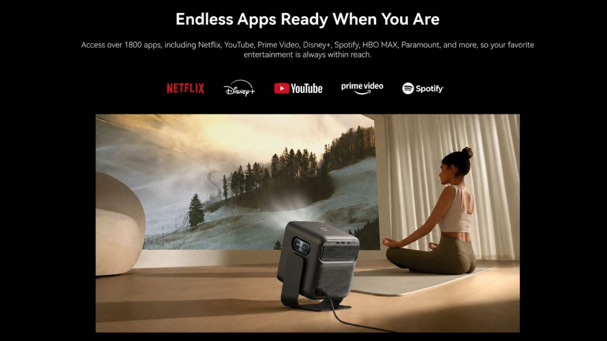 Mozart 1S projector displaying a mountain landscape in a room, next to a woman sitting on a mat.